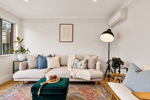 A modern living room with a sofa, ottoman, and a floor lamp. - Charming Sunlit Terrace in Vibrant Newtown (Newtown)