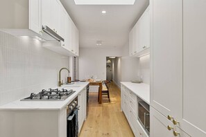 A narrow kitchen with white cabinetry, a gas stove, and a wooden dining table. - Charming Sunlit Terrace in Vibrant Newtown (Newtown)