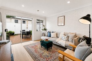 A modern living room with a sofa, coffee table, and a dining area with chairs and a table. - Charming Sunlit Terrace in Vibrant Newtown (Newtown)