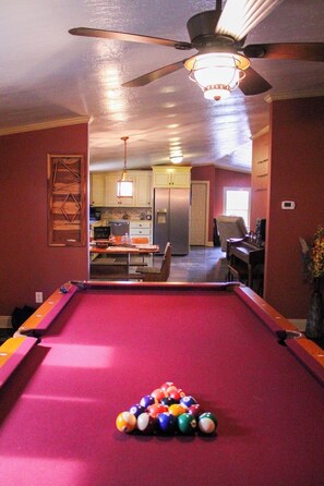 A pool table with balls, a ceiling fan, and a kitchen in the background.