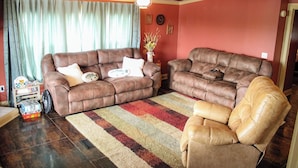 A living room with two brown leather sofas, a tan leather armchair, a striped rug, a ceiling fan, and a vase with flowers. - Lake Seminole Retreat with Boat Slip (Sneads)