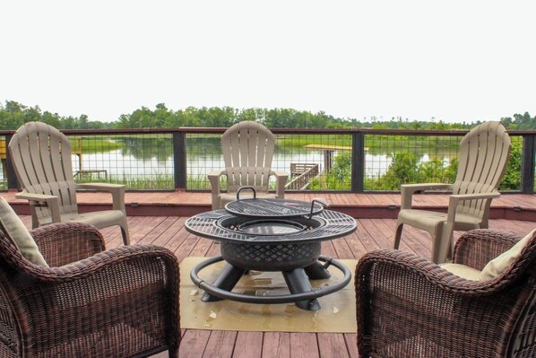 A deck with wicker chairs and a metal fire pit, overlooking a lake.