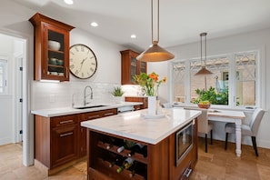 A modern kitchen with wooden cabinets, a large clock, a wine rack, and a dining area with a table and chairs. - Ocean & City View Retreat on the Riviera (Santa Barbara)