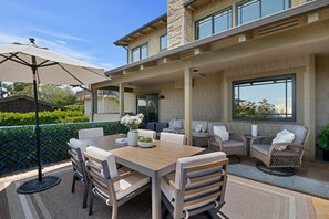 An outdoor patio with a dining table, chairs, a large umbrella, and wicker furniture. - Ocean & City View Retreat on the Riviera (Santa Barbara)