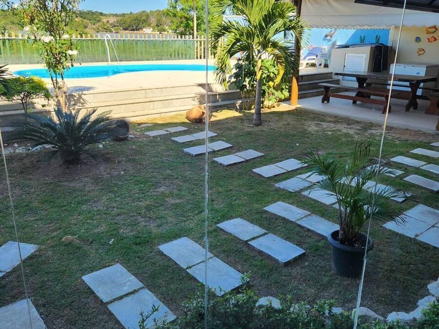 Uma área à beira da piscina com vista clara, um espaço coberto para relaxar e um alpendre com azulejos de pedra e plantas em vasos.