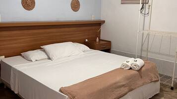Un dormitorio con cabecera de madera, cama con sábanas blancas, una manta marrón y una mesita de noche con lámpara.