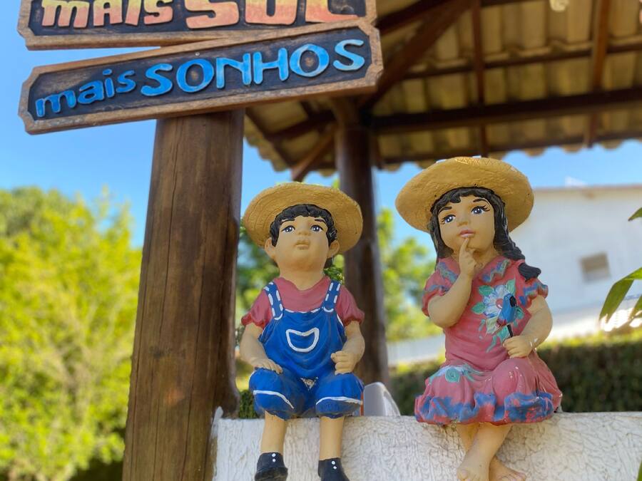 Un letrero de madera con texto en portugués, dos figuritas de niños y una estructura con techo de paja.