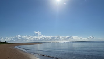 Uma praia com céu claro e reflexos de luz solar na água.