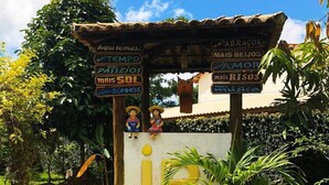 A garden area with a signpost, a large yellow letter 'I', and a small statue. - In Paradiso  (Aracruz)