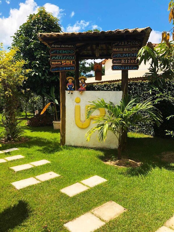 A garden area with a signpost, a large yellow letter 'I', and a small statue. - In Paradiso (Aracruz)
