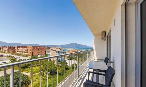 A balcony with a table and chairs, overlooking a residential area with buildings and a mountain in the distance. - Orikum Beachside Retreat Apartment 13 by Pikhost (Orikum)