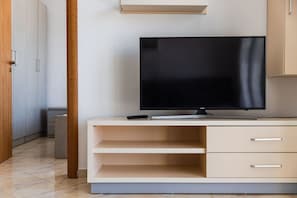 A modern room with a flat-screen TV on a white TV stand, a door, and a hallway. - Orikum Beachside Retreat Apartment 13 by Pikhost (Orikum)