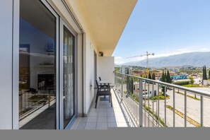 A balcony with a table and chairs, a glass door, and a view of a cityscape with mountains in the background. - Orikum Beachside Retreat Apartment 13 by Pikhost (Orikum)