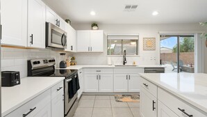 A modern kitchen with white cabinets, stainless steel appliances, and a large window. - Sunny Surprise Escape|Pool • Putting Green • Pets (Surprise)