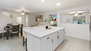 A modern kitchen with a central island, dining area with chairs, and a staircase leading to another level. - Sunny Surprise Escape|Pool • Putting Green • Pets (Surprise)