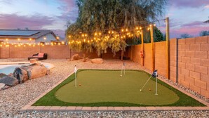 A backyard with a putting green, a hot tub, and string lights. - Sunny Surprise Escape|Pool • Putting Green • Pets (Surprise)