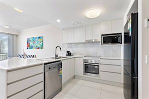 A modern kitchen with white cabinetry, stainless steel appliances, a dishwasher, and a microwave. - Miss A l e x l Beachfront Babe l Pool & Parking! (Alexandra Headland)
