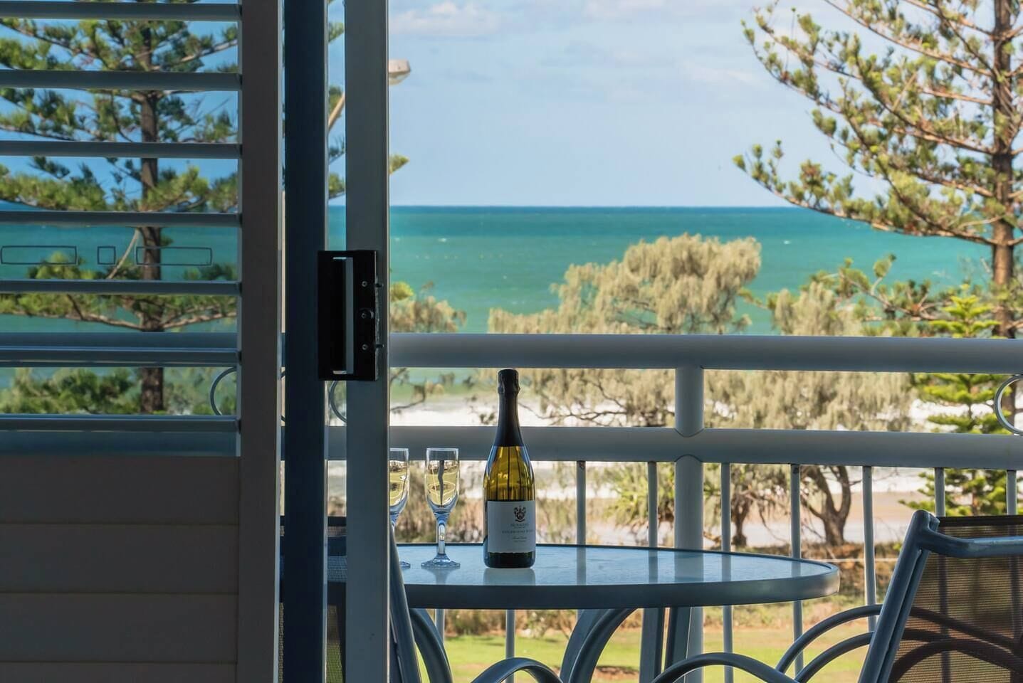 Un balcon avec une table, une bouteille de vin et deux verres.