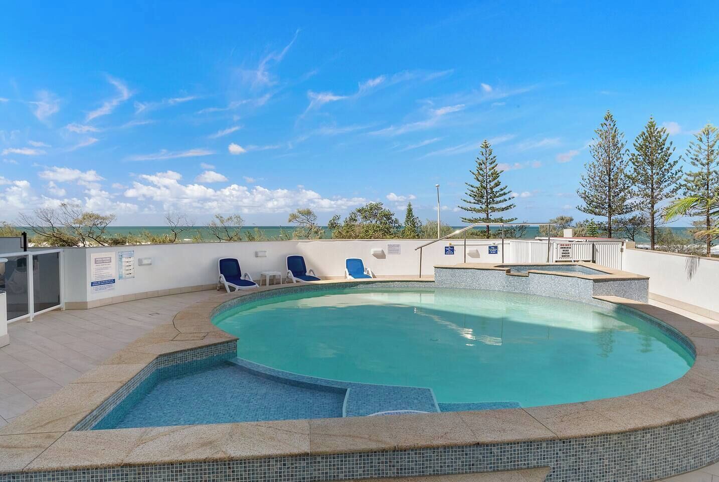 Una piscina con borde de azulejos, rodeada de sillones de descanso y vistas al océano.