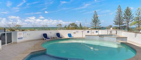 Una piscina con borde de azulejos, rodeada de sillones de descanso y vistas al océano.