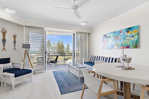 A room with a balcony, a round table, and a painting. - Miss A l e x l Beachfront Babe l Pool & Parking! (Alexandra Headland)