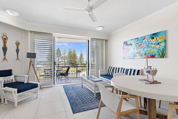 A room with a balcony, a round table, and a painting. - Miss A l e x l Beachfront Babe l Pool & Parking! (Alexandra Headland)