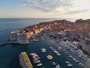 A coastal town with a historic fortification, a harbor with numerous boats, and a dense cluster of buildings. - Apartment Marble View (Dubrovnik)