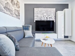 Ein modernes Wohnzimmer mit einem grauen Sofa, einem weißen Couchtisch und einem großen Flachbildfernseher, der an einer grauen Wand angebracht ist.