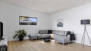 Uma sala de estar moderna com sofá em formato de L, mesa de centro, luminária de chão e uma grande janela com vista para uma casa.