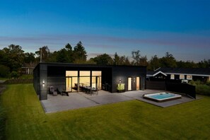 Ein modernes Haus mit Terrasse, Whirlpool und gepflegtem Rasen.