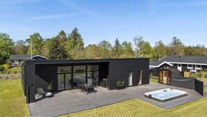 Uma casa moderna com um deck, área de estar externa e uma banheira de hidromassagem.