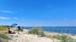 Ein Strand mit Menschen, die sich sonnen und schwimmen, einem klaren, blauen Himmel und einem ruhigen Meer.