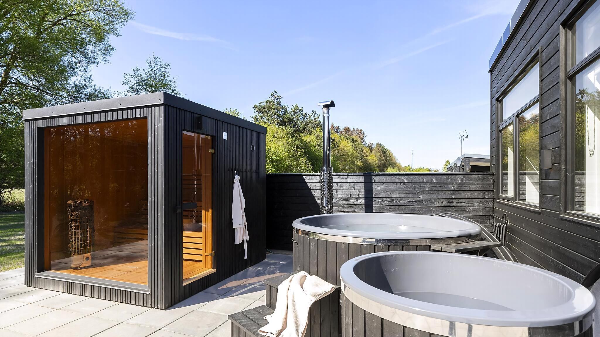 Un espace de détente extérieur moderne, doté d’un sauna, de deux bains à remous et d’une terrasse en bois.