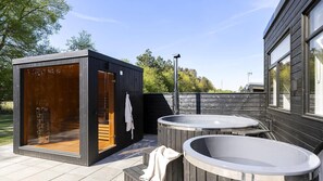 Ein moderner Außen-Wellnessbereich mit Sauna, zwei Whirlpools und einer Holzterrasse.