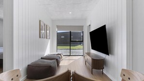 Ein modernes Interieur mit einer großzügigen Sitzecke, einem Flachbildfernseher und Blick durch eine Glastür.
