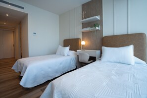 Et hotelværelse med to senge, et skrivebord og en lille plante.