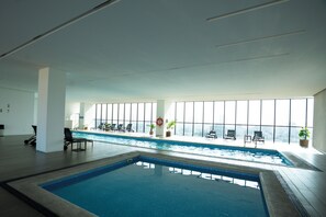 An indoor swimming pool with a view of the city, lounge chairs, and potted plants. - Modern & Comfortable Apartment (Guadalajara)