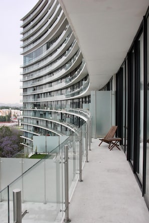 Ein modernes Gebäude mit einem geschwungenen Balkon, Glasgeländern und einem Holzstuhl.