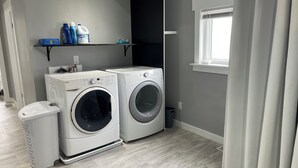 Un lavadero con dos lavadoras, un cubo de basura y un estante con productos de limpieza.