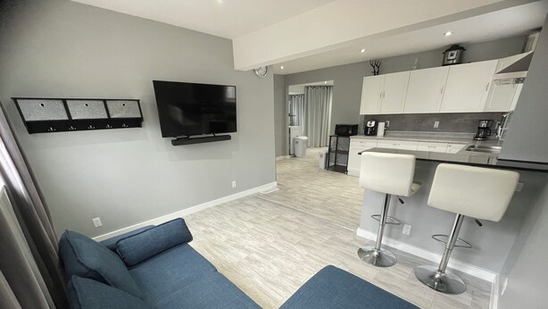 Una sala de estar moderna con un televisor de pantalla plana, un sofá y una zona de cocina con armarios blancos y un taburete de bar.