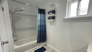 Un baño con ducha de vidrio, una bañera, un perchero con toallas y una ventana.