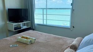 Een hotelkamer met een bed, een televisie, een raam met uitzicht op zee en een gordijn.