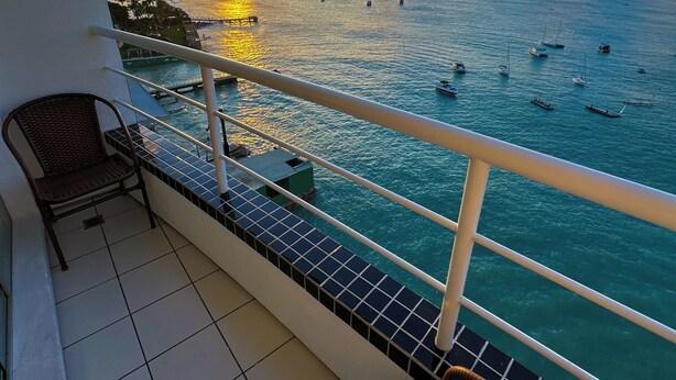 Een balkon met uitzicht op zee, een stoel en een betegelde vloer.