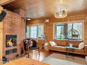 Ein gemütliches Zimmer mit Kamin, Holzwänden, einer Couch und einer Hängelampe.