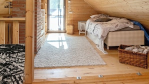 Un dormitorio con techo inclinado, una cama con ropa de cama estampada, una cesta de mimbre y una vista por una puerta.
