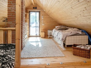 A bedroom with a sloped ceiling, a bed with patterned bedding, a wicker basket, and a view through a door.