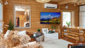 Interior acogedor de una cabaña con paredes de madera, un espejo grande, un televisor montado, una mesa de comedor y una zona de cocina.