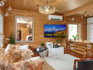 A cozy cabin interior with wooden walls, a large mirror, a mounted TV, a dining table, and a kitchen area.