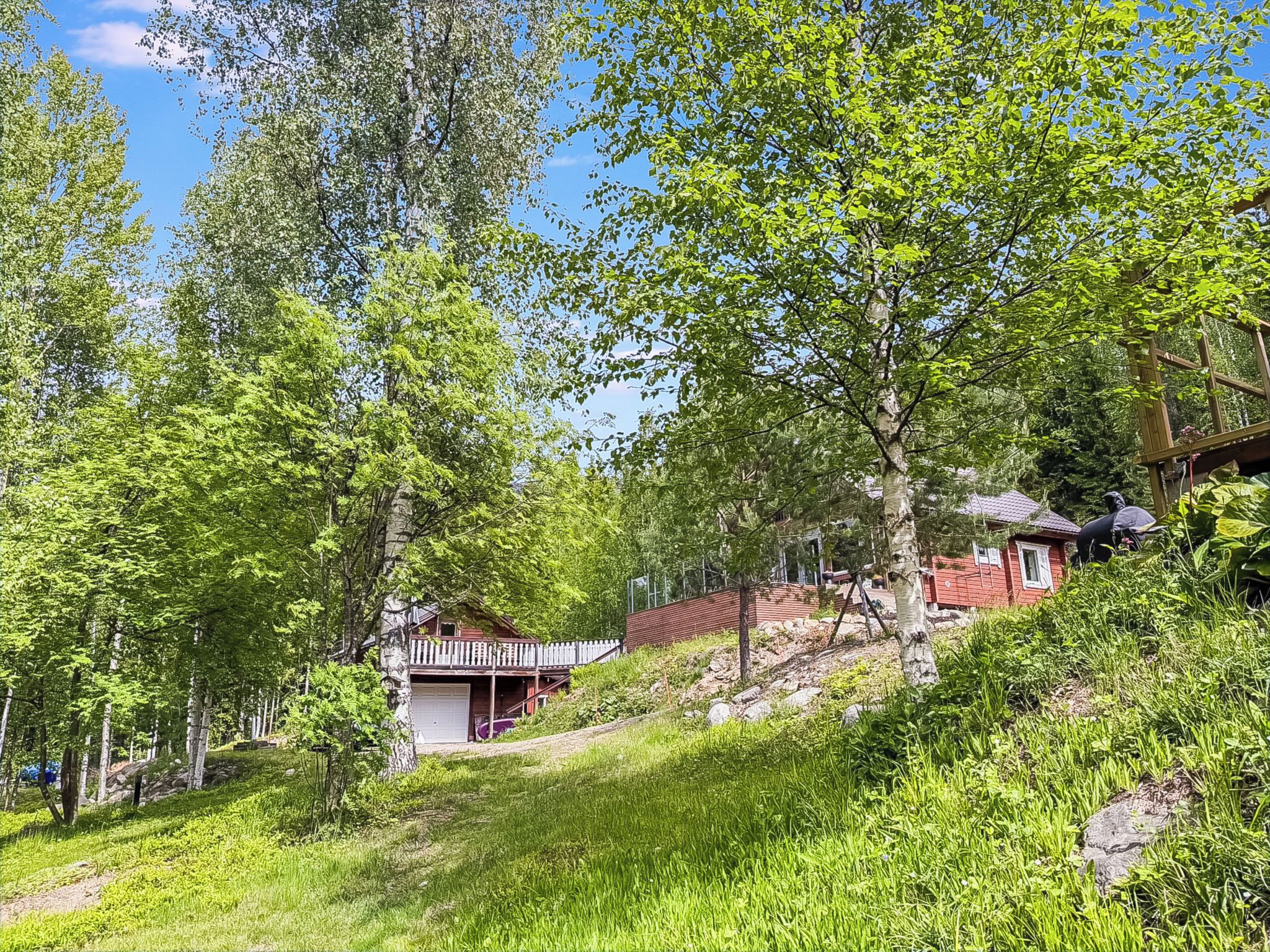 Una baita rossa con un balcone, immersa nel verde e circondata da alberi.