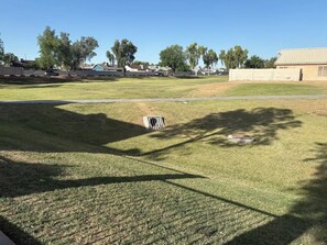 A grassy area with a drainage grate, a paved path, and a building in the background.